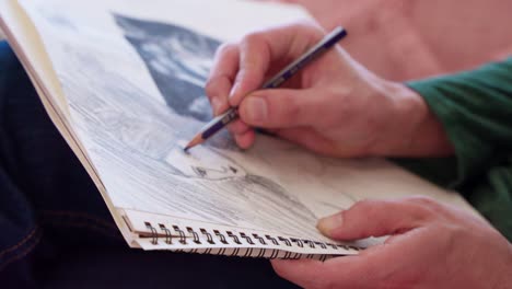 Close-up-of-hispanic-artist's-hand-drawing-woman's-portrait-on-sketch-pad-while-sitting-on-pink-couch