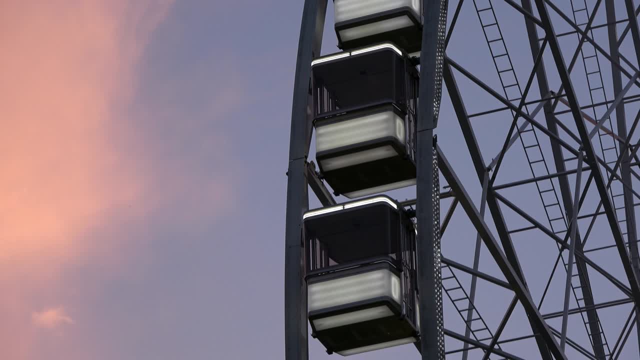4K. The cabins of a ferris wheel that this stop are hanging. It´s sunset