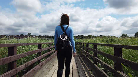 cinematic shot of a woman walking on a lagoon dock, the wind moves her hair and the environment