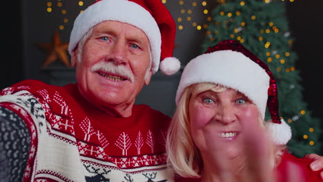 Mature-couple-family-in-Santa-Claus-hats-celebrating-Christmas-looking-at-camera-and-hugging-at-home