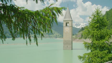 Close-up-shot,-Tree-branch-blow-by-the-wind-in-Italy,-Kirchturm-von-Altgraun-and-People-walking-on-the-sun-bar-on-a-bright-sunny-day-in-the-background