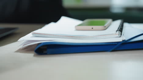 close up of person dropping folder on desk with smartphone placed on top, beside open laptop and small decorative plant in modern workspace