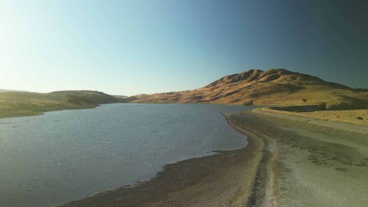 An ascending drone view captures the expansive Paicines Reservoir, framed by open plains and scattered trees in the heart of California.