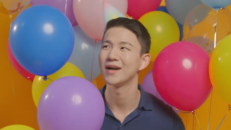 Retrato-De-Estudio-De-Un-Hombre-Vestido-Con-Sombrero-De-Fiesta-Celebrando-Un-Cumpleaños-Escondido-Detrás-De-Globos