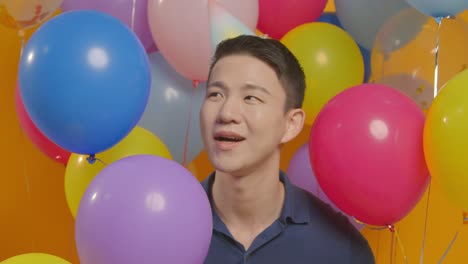 파티 모자를 입은 남자가 풍선 뒤에 숨어 생일을 축하하는 스튜디오 초상화