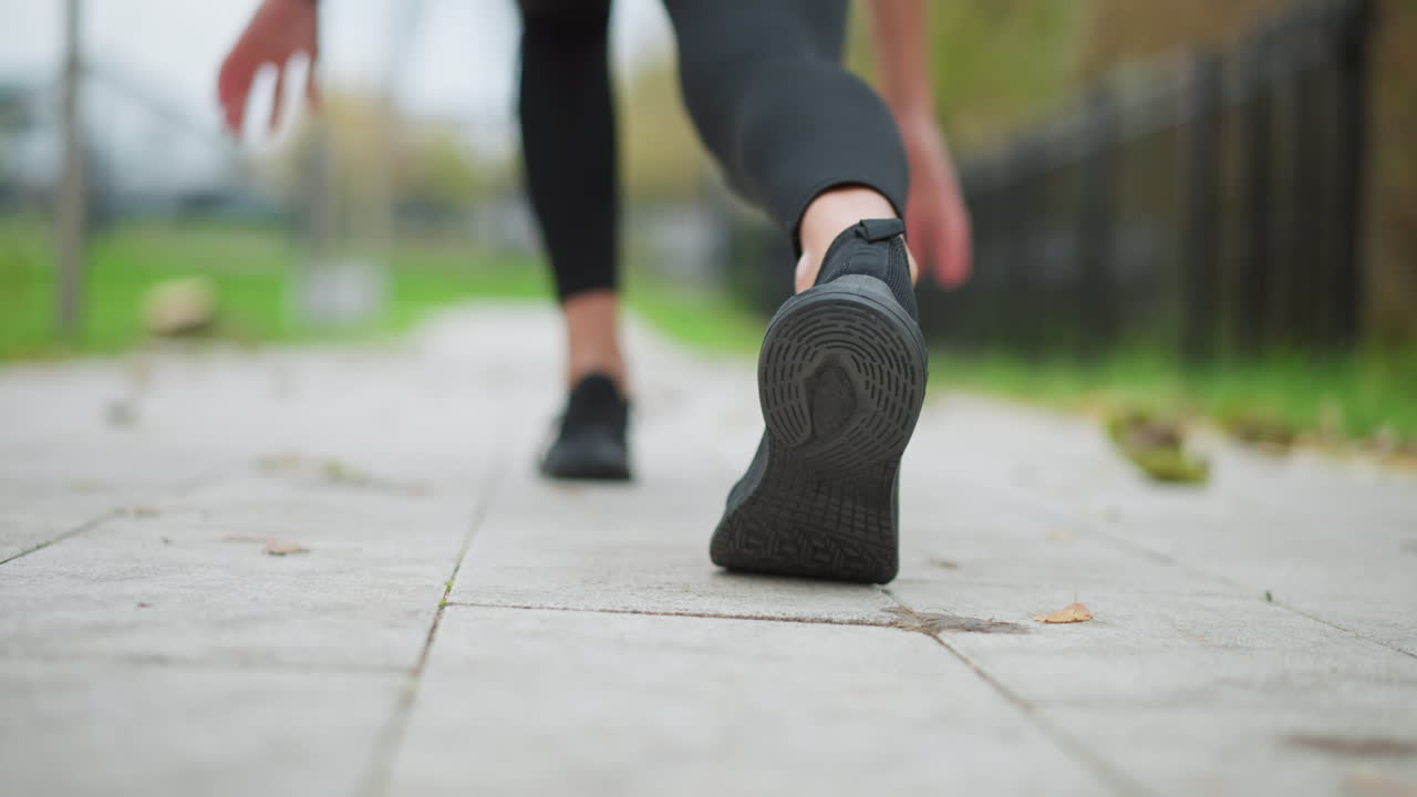 Vista borrosa de la pierna de un corredor con zapatillas negras, agachándose en el pavimento, preparándose para correr, una toma de estilo de vida activo al aire libre que se centra en la pierna y el pie en movimiento, listo para el ejercicio o los deportes.