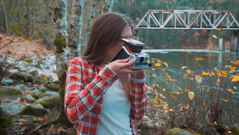 Photographer-woman-takes-Polaroid-photo-along-riverside-among-fall-colors