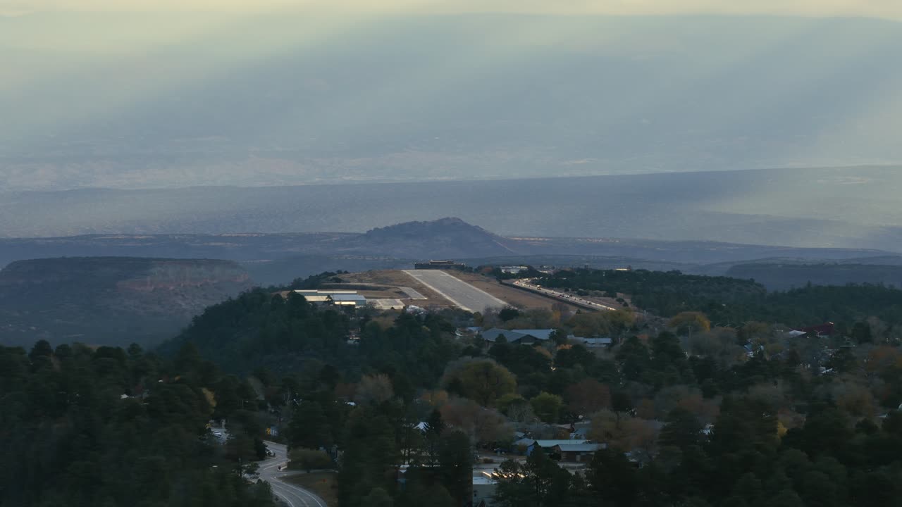 Telephoto orbit of Los Alamos Airport with sweeping canyon layers and soft sunrise rays. Ideal for aviation, travel, science, and cinematic landscape themes