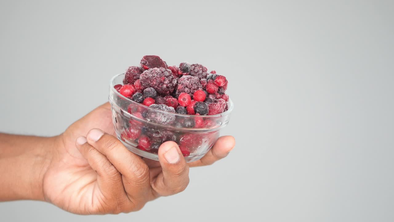Mano che tiene una ciotola di frutti di bosco misti congelati