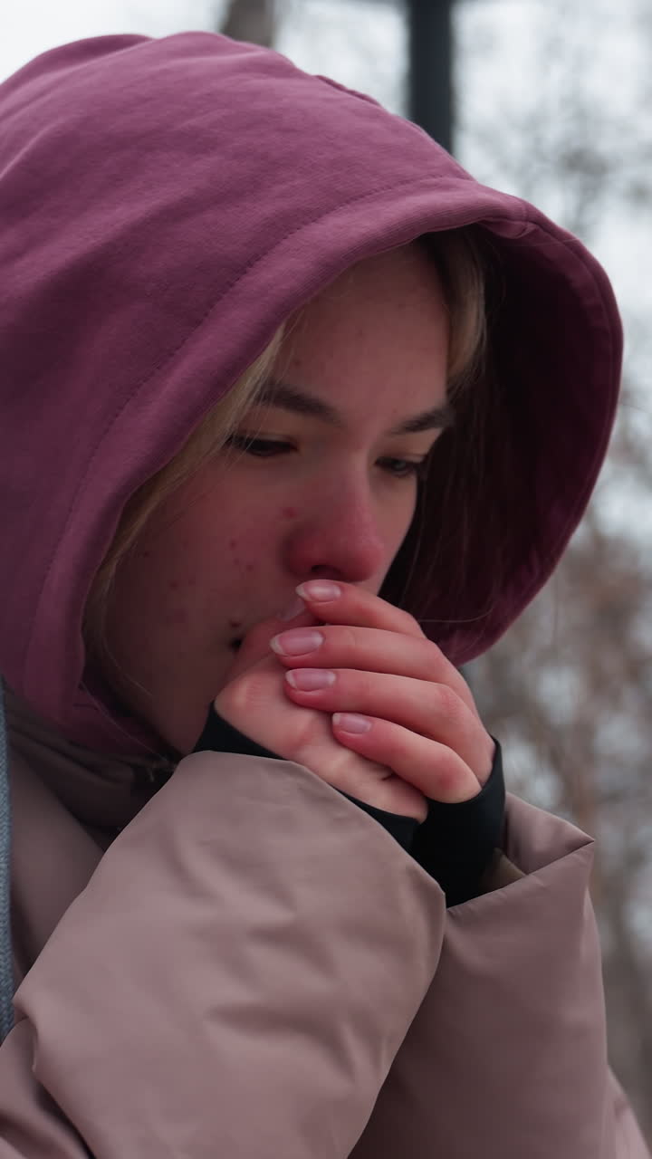 primer plano de una mujer que siente frío mientras ajusta su sudadera con capucha mientras camina al aire libre en invierno, está envuelta en una chaqueta gruesa, apoyándose contra el aire frío, rodeada de árboles desnudos