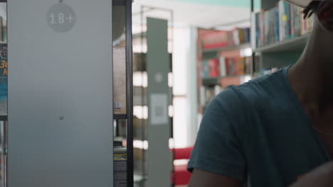 Academician walking through library aisle carrying large stack of books in arms, surrounded by shelves filled with colorful literature, creating academic and intellectual atmosphere
