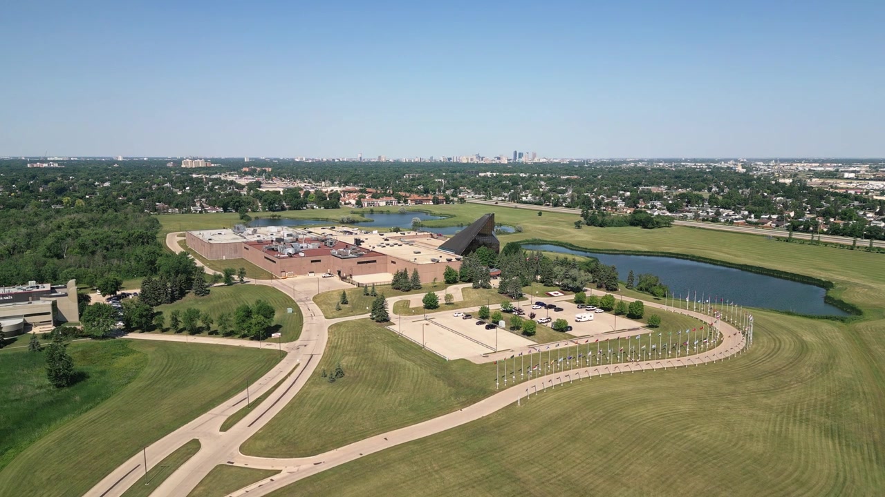 Ripresa aerea lenta in avanti con drone dei terreni della Zecca Reale Canadese a Winnipeg con bandiere, strade, giochi d'acqua e lo skyline del centro in una giornata estiva