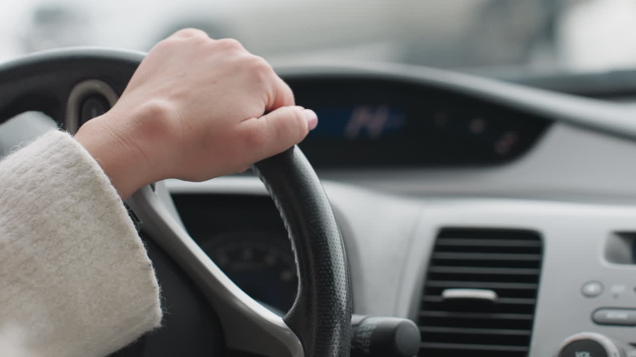 Close up rear view of driver wearing winter coat hands on steering wheel during snowy road trip with blurred dashboard indicator lights and frosty window