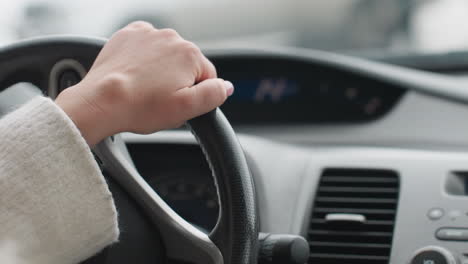close up rear view of driver wearing winter coat hands on steering wheel during snowy road trip with blurred dashboard indicator lights and frosty window