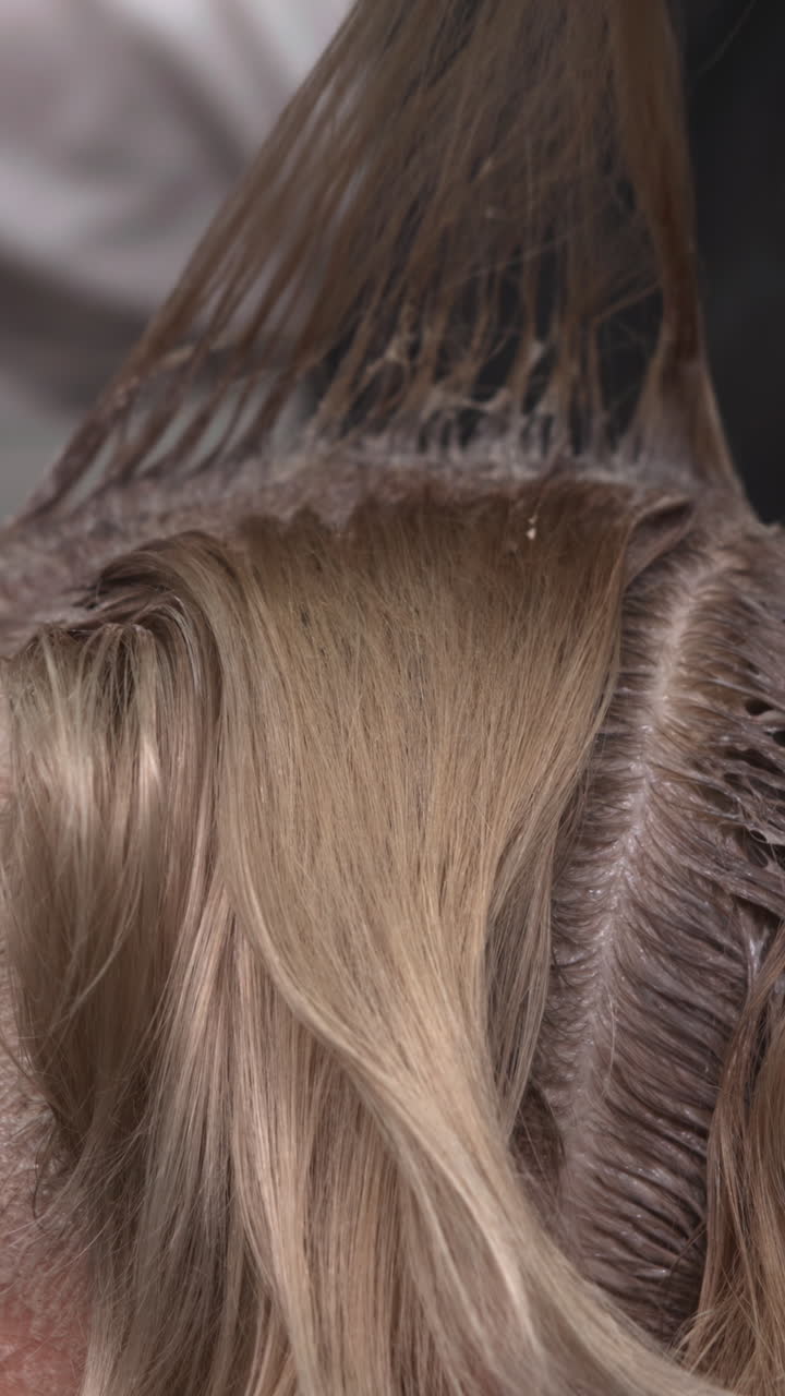 Profilo laterale di stilista che esegue balayage e colora le radici su cliente bionda caucasica, con guanti rosa, riga visibile. Media