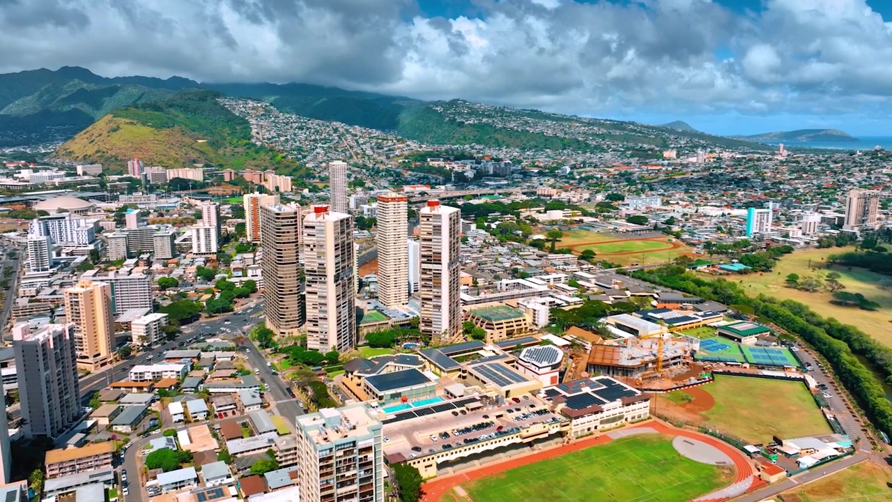 Toàn cảnh ngoạn mục của Honolulu, Hawaii, Hoa Kỳ với nền là những ngọn núi xanh phía sau. Mây trắng bồng bềnh phủ kín bầu trời. Góc nhìn từ trên cao
