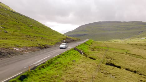 a white car driving on a scenic road in the faroe islands, surrounded by lush green hills