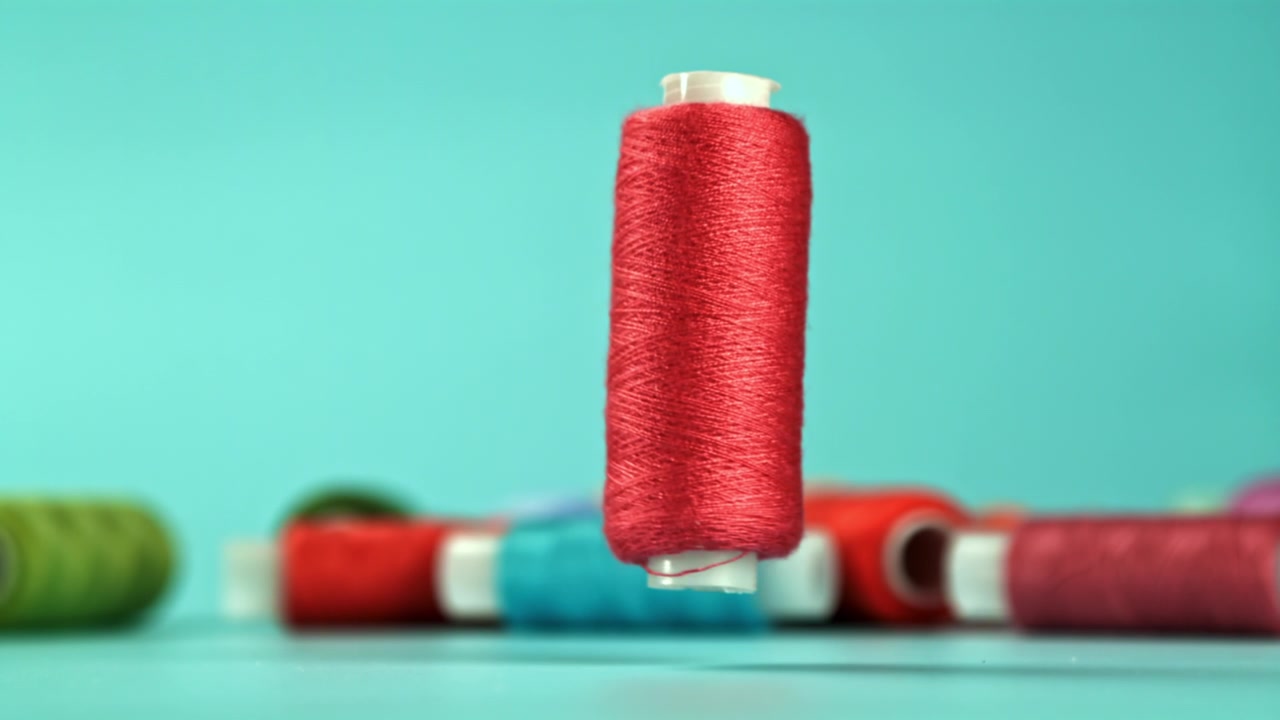 Red Thread Spool Falling in Slow Motion on Blue Background