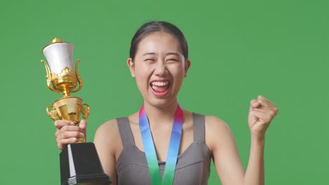 close up of asian woman with a gold medal and trophy screaming goal celebrating winning as the first winner on green screen background in the studio