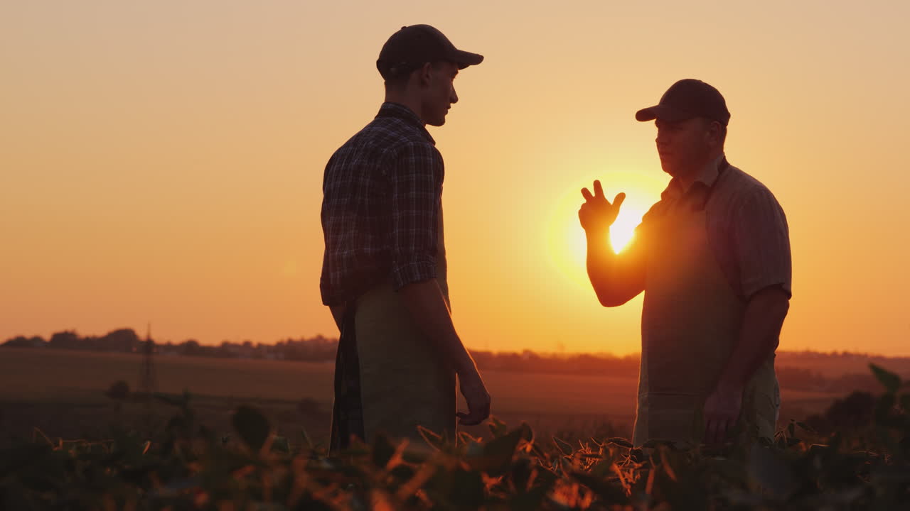 Un agricoltore anziano stringe la mano a un giovane collega, sorriso, emozioni positive.