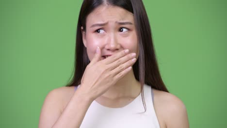 young beautiful asian businesswoman covering mouth while looking guilty