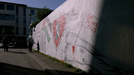 a person walks past a free palestine mural in downtown reykjavik during a sunny day