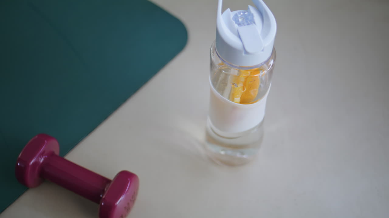 Unknown athlete taking water bottle with lemon placed at gym floor closeup