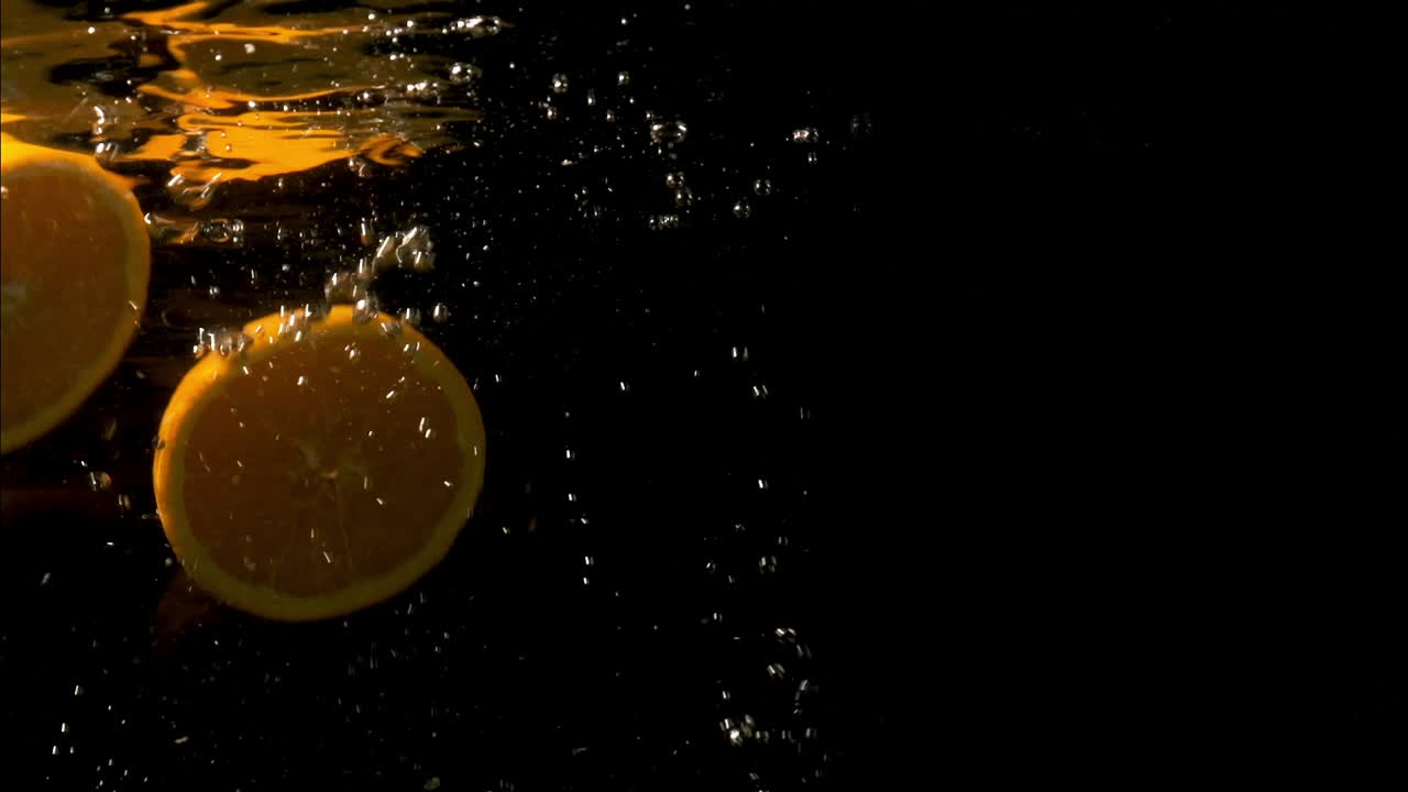 Arancia tagliata a metà che cade nell'acqua limpida causando bolle.