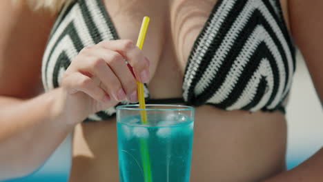 attractive woman in bikini shatters ice in a cocktail, close-up shot.