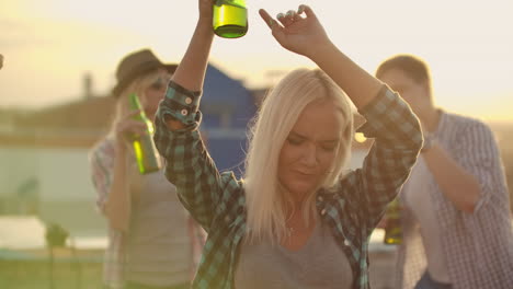 the russian blonde is dancing on the roof with her friends on the party. she closes her eyes and moves her hands in dance with beer.