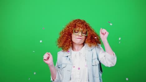 young happy redhead curly woman jumping and throwing confetti, dancing over green chroma key background, slow motion