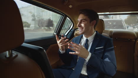 Smiling-businessman-sharing-news-in-voice-message-to-mobile-phone-in-automobile.