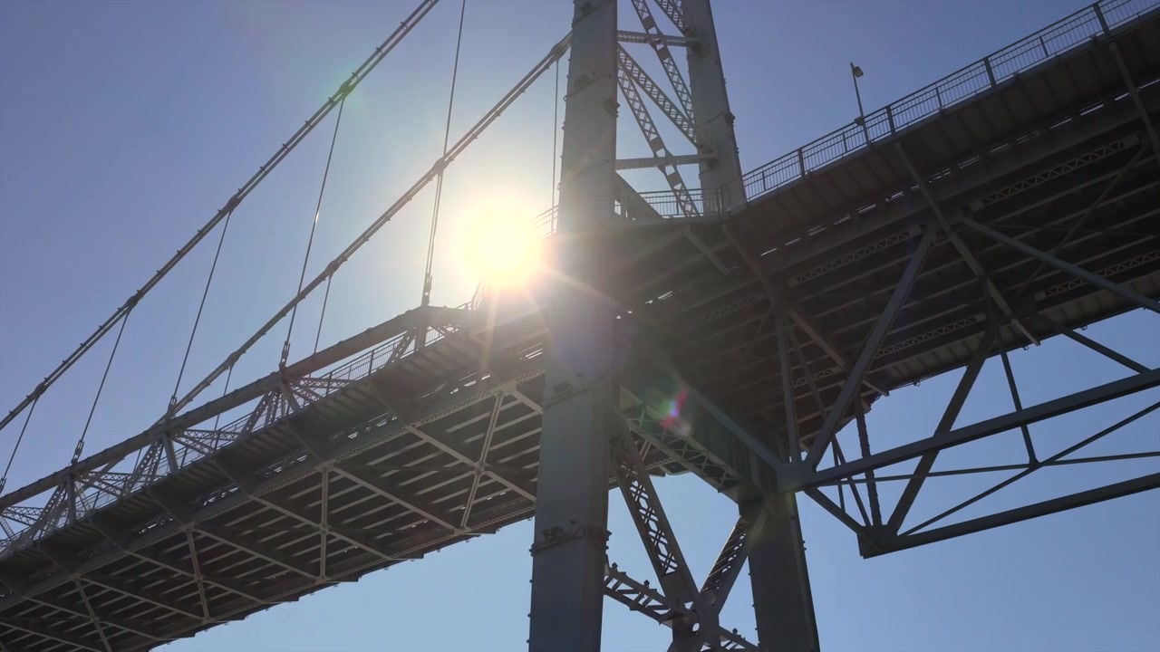 The Hercílio Luz Bridge spans across the water, silhouetted against the bright sun in Florianopolis, Brazil. Ideal for travel documentaries or infrastructure studies.