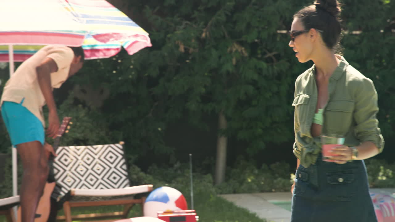 Woman in sunglasses holding drink, talking by poolside, enjoying sunny day