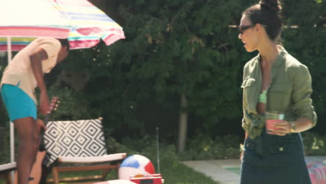 woman in sunglasses holding drink, talking by poolside, enjoying sunny day