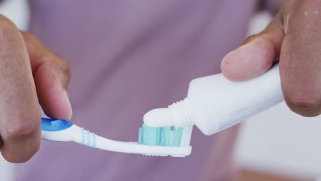 close up of hands of biracial man applying toothpaste to toothbrush in bathroom, slow motion