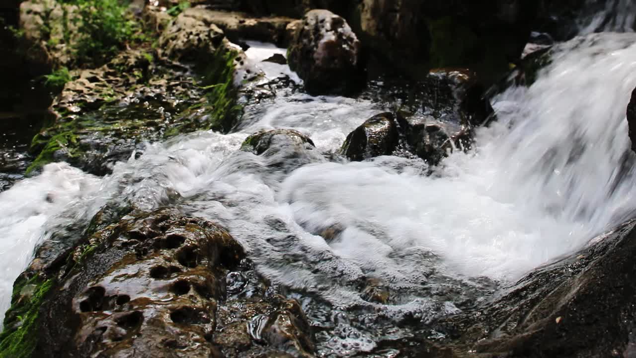 agua que cae suavemente en cascada desde el lecho de un pequeño arroyo que pasa sobre las rocas y luego continúa cayendo sobre otro borde