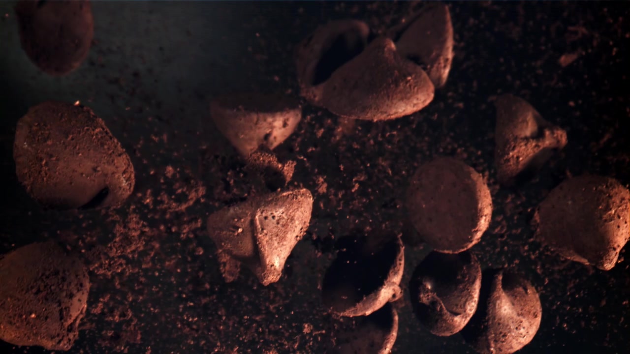 Chispas de chocolate cayendo en cámara lenta sobre cacao en polvo oscuro