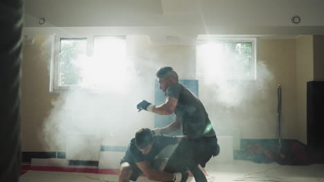 guy lifts and throws partner on sports club floor. young man attacks friend exercising during sparring in foggy gym slow motion. martial arts training