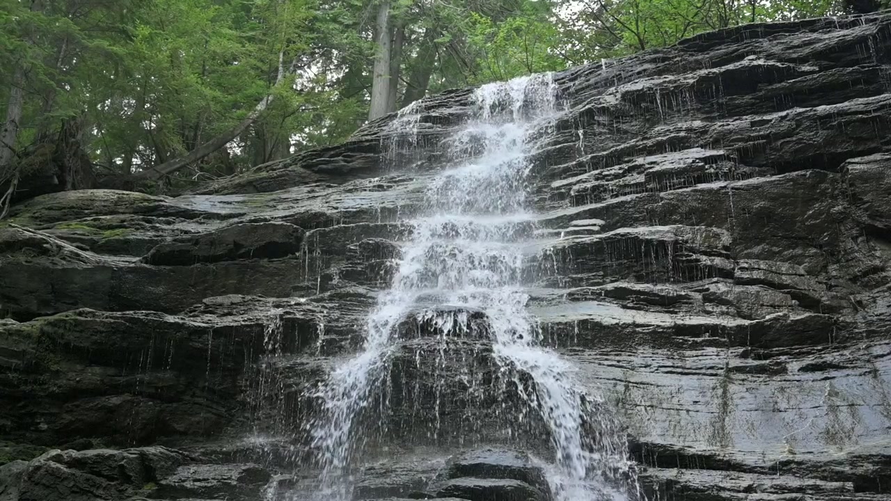 Statisk bilde av en foss i sakte film som fosser ned en steinete klippe i et frodig skoglandskap ved Moose Falls, Revelstoke, som fremhever storslått naturskjønnhet og ro
