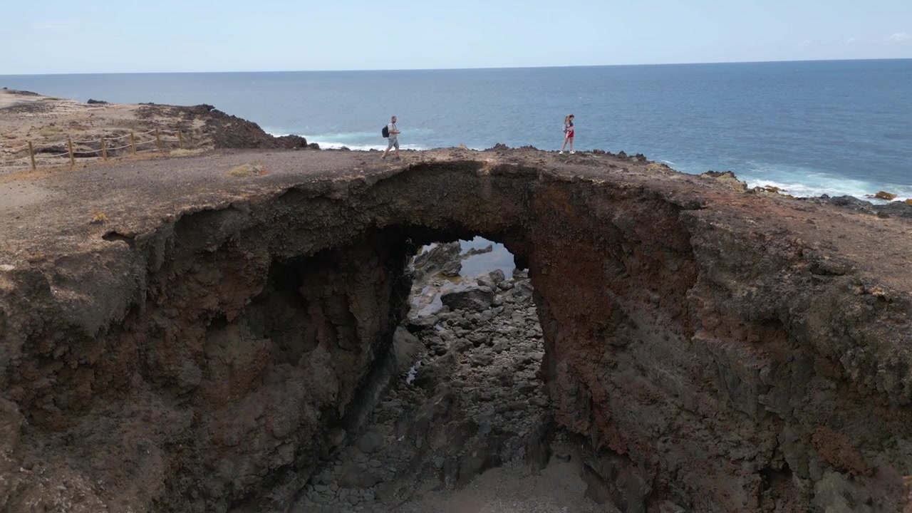 Persone esplorano un arco vulcanico sopra una costa rocciosa con vista sull'oceano a Tenerife, Spagna