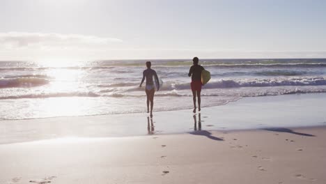 african american couple running with surfboards on the beach