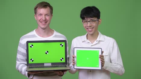 two happy young multi-ethnic businessmen showing laptop and digital tablet to the camera