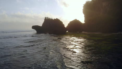 Incredible-footage-of-a-rocky-shore-covered-with-algae,-blue-ocean---sunrise-behind-large-rocks-at-the-coast-–-magical-lights