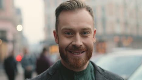 portret van een gelukkige blanke zakenman met een baard die in de herfst vrolijk naar de camera glimlacht op straat