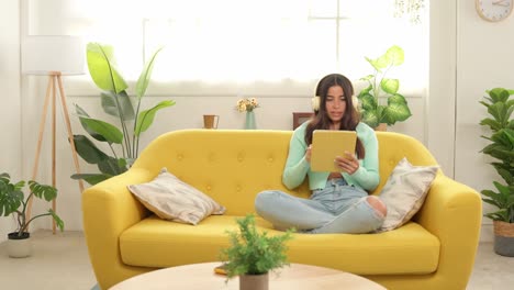 woman using tablet on yellow sofa at home