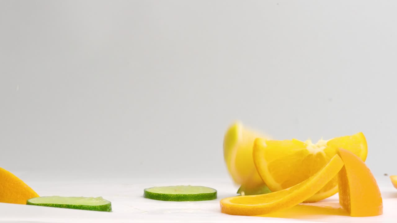 rodajas y rodajas de cítricos de limón, lima y naranja caen en una pila y salpican jugos sobre fondo blanco en cámara lenta
