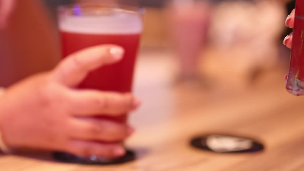 Close-up of hands grasping red beverages on a wooden table with coasters.