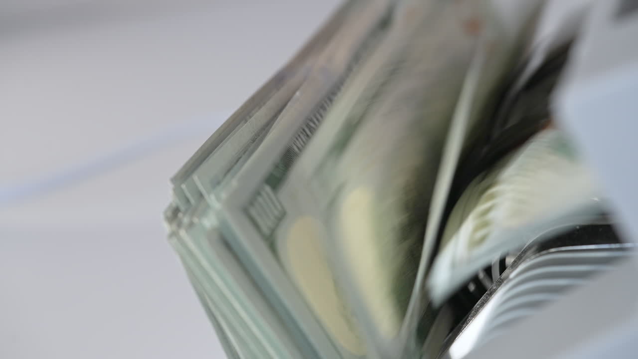 Quickly counted one hundred dollar bills in money counting machine. Rotating mechanism of equipment close up. Blurred backdrop.