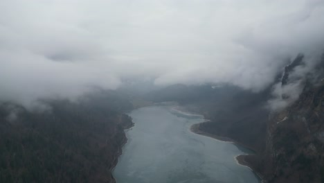 espesas nubes de niebla se asientan en el valle que envuelve un lago congelado o un embalse en los alpes.